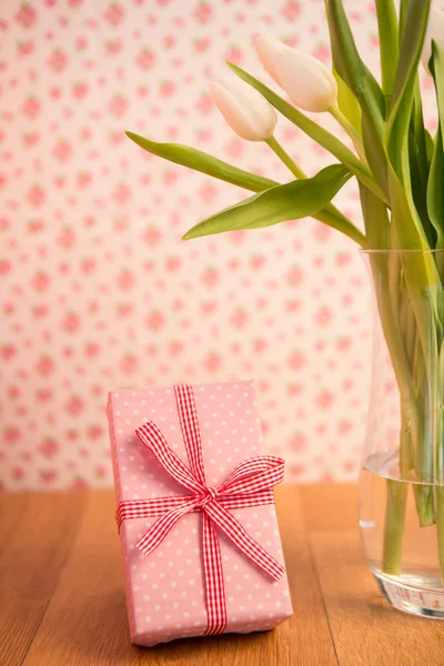 Vase of tulips on wooden table with pink wrapped gift Royalty Free Stock Images