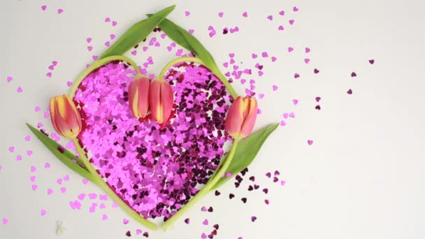 Licht schijnt over hart gemaakt van roze confetti omlijst door tulpen — Stockvideo