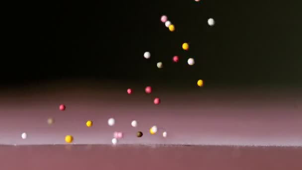 Hagelslag gieten op roze oppervlak op zwarte achtergrond — Stockvideo