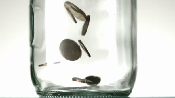 Many coins pouring into glass jar close up on white background — Stock Video