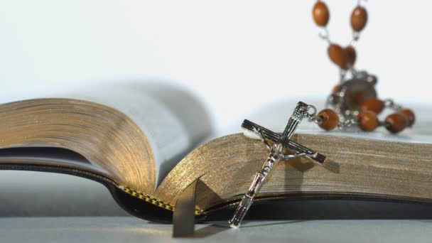 Rozenkrans kralen vallen op open Bijbel op witte achtergrond close-up — Stockvideo