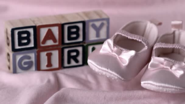 Baby booties falling on pink blanket with baby girl message in blocks — Stock Video