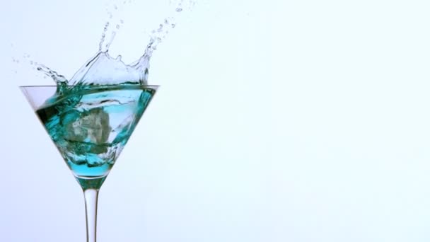 Ice falling into cocktail glass of blue alcohol on white background — Stock Video