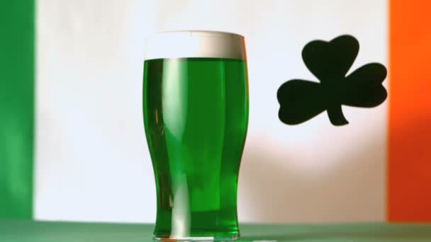 Large green shamrock falling beside pint of green beer — Stock Video