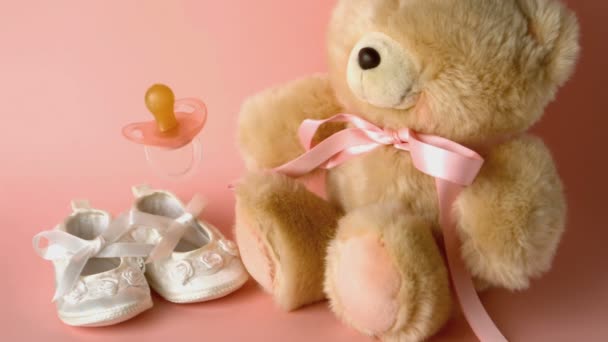 Pink soother falling in front of baby shoes and a teddy bear — Stock Video