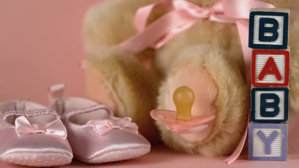 Pink soother falling besides baby shoes, blocks and teddy bear — Stock Video