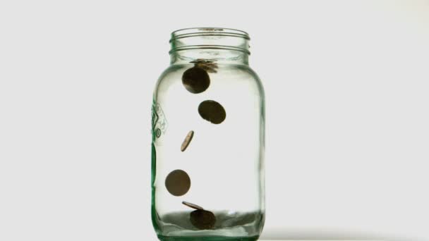 Coins pouring into glass jar on white background — Stock Video