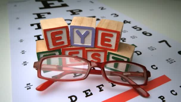 Glasses falling onto eye test with wooden blocks spelling out eye test — Stock Video