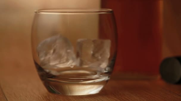 Pinzas que colocan hielo en el vaso y whisky que se vierte — Vídeo de stock