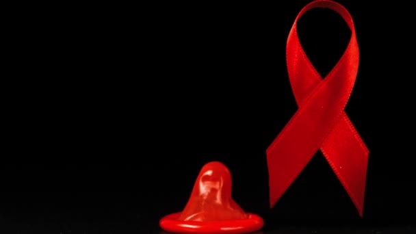 Condom falling over in front of a red ribbon on black background — Stock Video