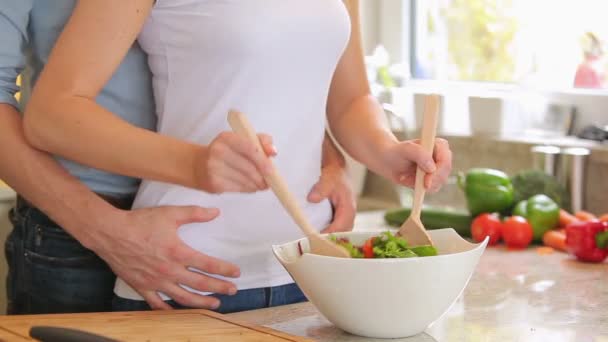 Woman mixing salad with man holding her from behind — Stock Video