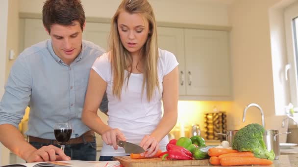 Mujer cortando verduras con hombre leyendo libro de cocina — Vídeos de Stock