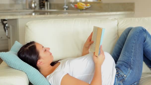 Mujer embarazada leyendo un libro en el sofá — Vídeos de Stock