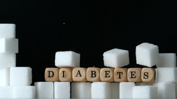 Sugar cubes and dice spelling diabetes falling down in black background over sugar cubes wall — Stock Video