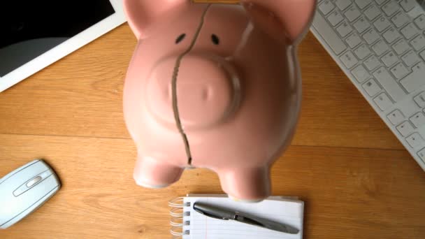 Piggy bank falling on a desk beside tablet pc and keyboard — Stock Video