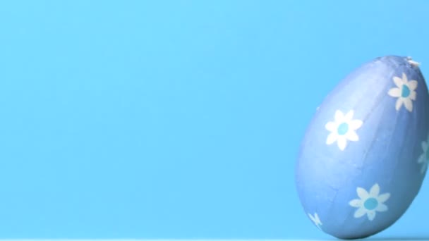Блакитне пасхальне яйце котиться на синьому фоні — стокове відео