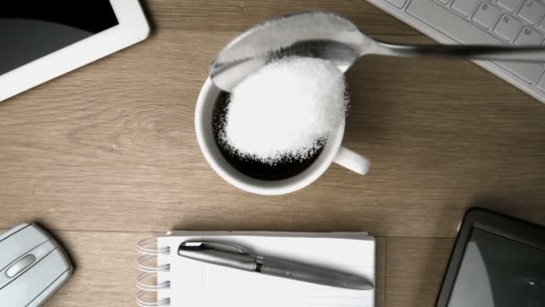 Sugar in teaspoon falling into cup of coffee on a desk — Stock Video