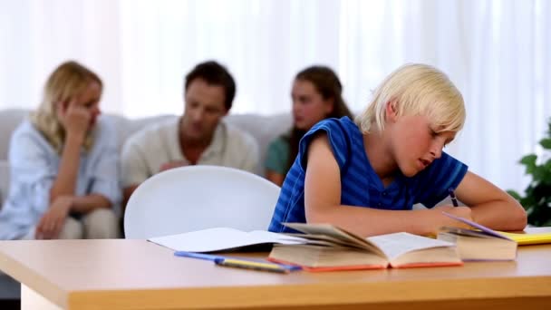 Filho fazendo seu dever de casa com a família no sofá atrás — Vídeo de Stock