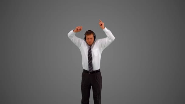 Businessman jumping and listening to music on headphones on grey background — Stock Video