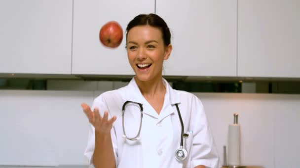 Enfermera en casa lanzando y atrapando manzana y sonriendo en la cocina — Vídeos de Stock