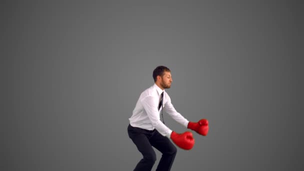 Бизнесмен в боксёрских перчатках прыгает и бьет на сером фоне — стоковое видео