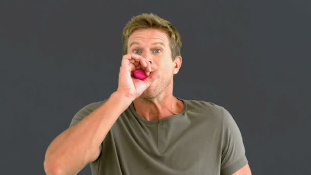 Чоловік дме рожевий конфетті на сірому екрані — стокове відео