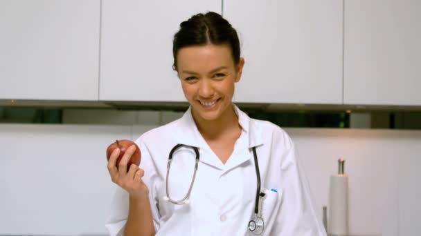 Enfermera en casa sosteniendo manzana y sonriendo en la cocina — Vídeos de Stock