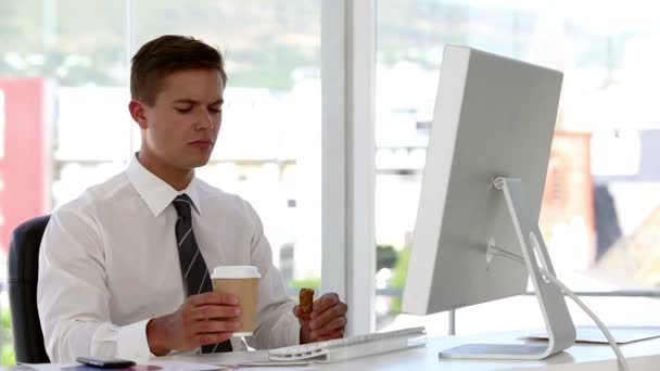 Joven hombre de negocios comiendo y bebiendo mientras trabaja en su computadora — Vídeos de Stock