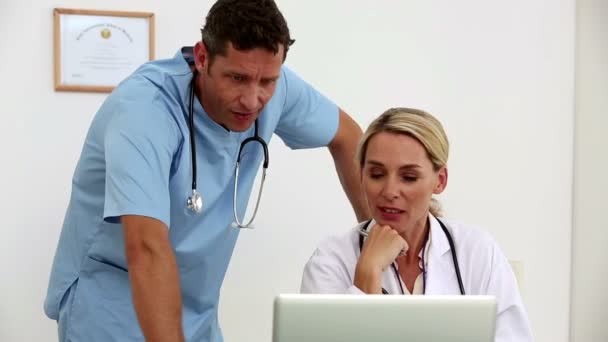Dois médicos usando um laptop juntos em seu escritório — Vídeo de Stock