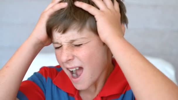 Раздражённый мальчик держит голову между рук — стоковое видео