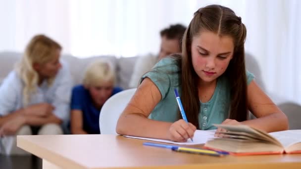 Hija haciendo su tarea con la familia en el sofá detrás — Vídeos de Stock