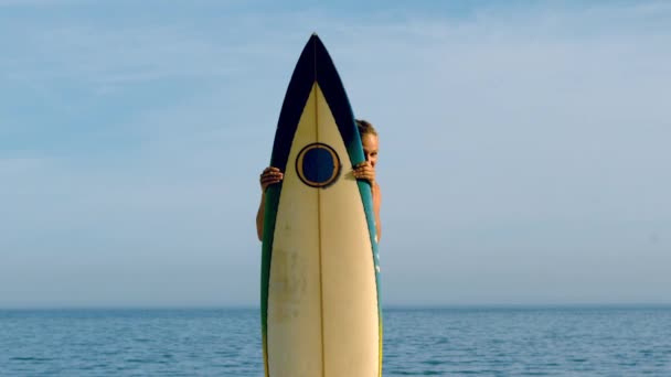 Female surfer peeking from behind her board — Stock Video