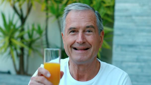 Hombre jubilado brindando con jugo de naranja afuera — Vídeos de Stock