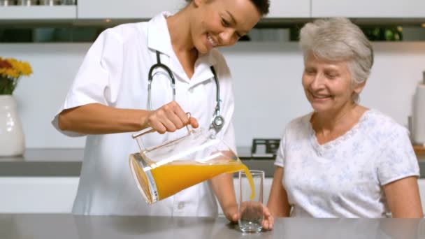 Home help pouring orange juice for patient in kitchen — Stock Video