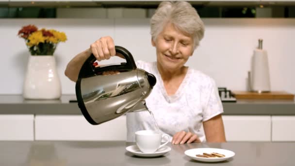 Elderly woman pouring boiling water from kettle into cup in kitchen — Stock Video