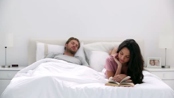 Kobieta, czytanie książki, podczas gdy partner śpi — Wideo stockowe