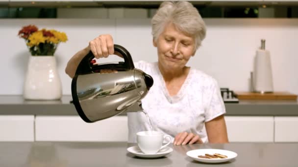 Συνταξιούχος γυναίκα ρίχνει βραστό νερό από το βραστήρα σε φλυτζάνι στην κουζίνα — Αρχείο Βίντεο