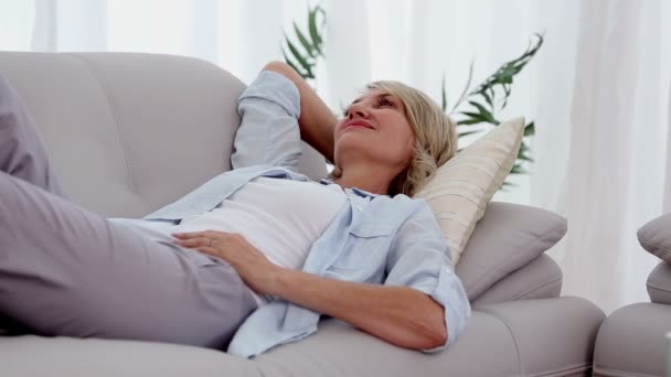 Mujer sonriendo y relajándose en el sofá — Vídeos de Stock