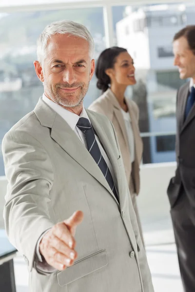 Businessman giving a handshake with colleagues behind — Stock Photo, Image