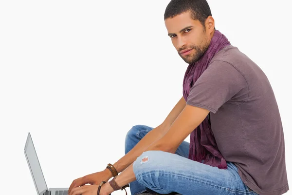 Serious man wearing scarf sitting on floor using laptop — Stock Photo, Image