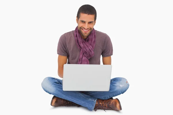 Homem elegante sentado no chão usando laptop e sorrindo para a câmera — Fotografia de Stock