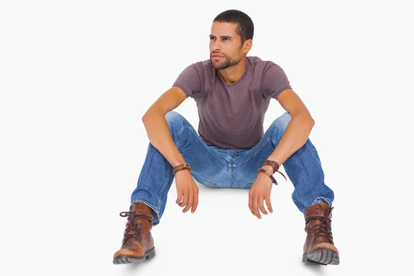 Hombre guapo sentado en el suelo y mirando hacia otro lado —  Fotos de Stock