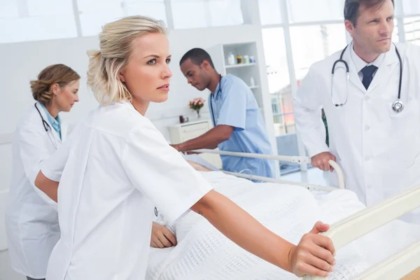 Serious doctors about to walk with patient bed — Stock Photo, Image