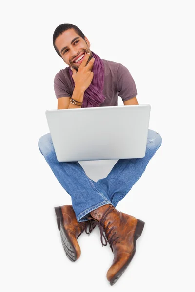 Myślący człowiek siedzi na podłodze za pomocą laptopa i uśmiechając się — Zdjęcie stockowe