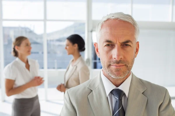 Seriöser Geschäftsmann steht, während Kollegen gemeinsam diskutieren — Stockfoto