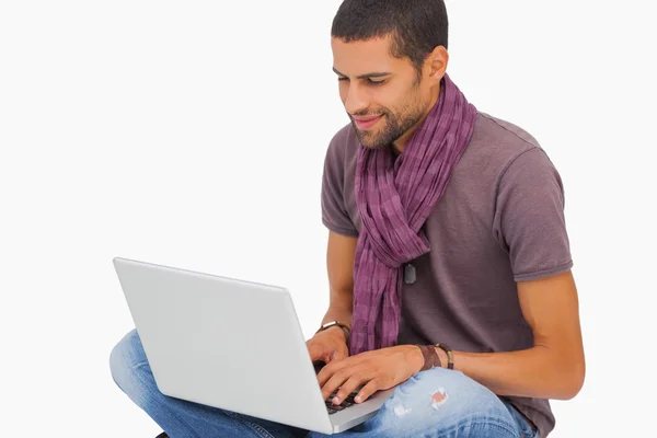 Uomo sorridente seduto sul pavimento utilizzando il computer portatile — Foto Stock