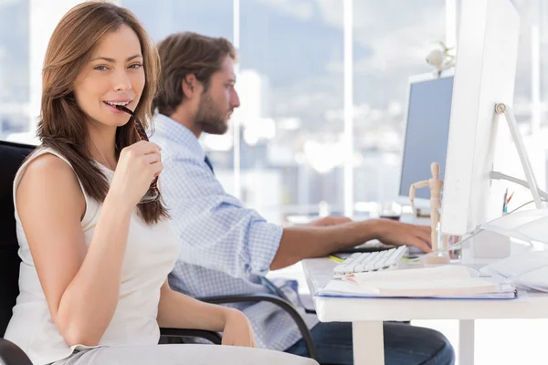 Woman biting her glasses with colleague working behind — Stock Photo, Image