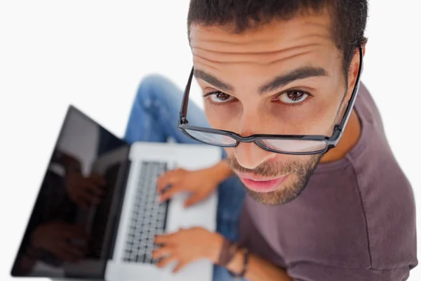 Homem usando óculos sentado no chão usando laptop e olhando para a câmera — Fotografia de Stock