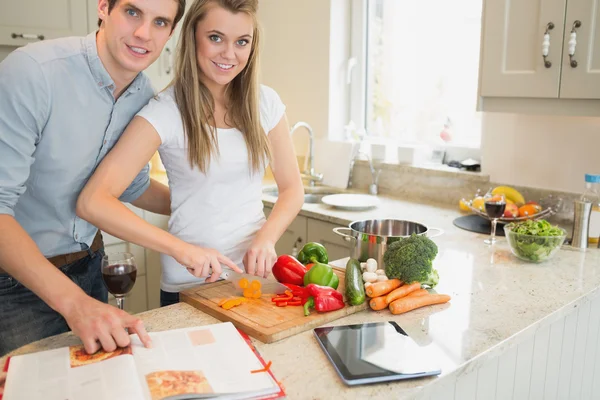 Vrouw snijden groenten met man leest de kookboek — Stockfoto