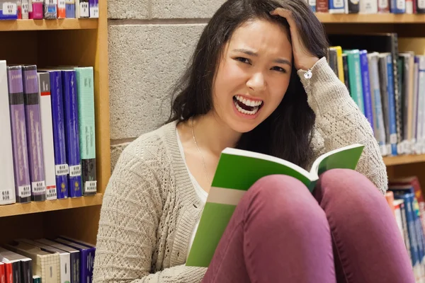 Estudante estressado lendo em uma biblioteca — Fotografia de Stock